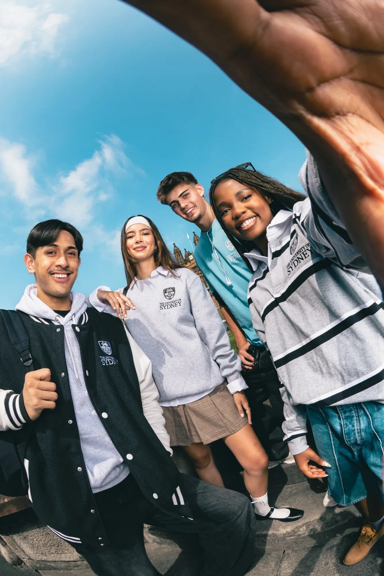 Wide-angle shot of four students in University of Sydney sweaters and a varsity jacket smiling into the lens