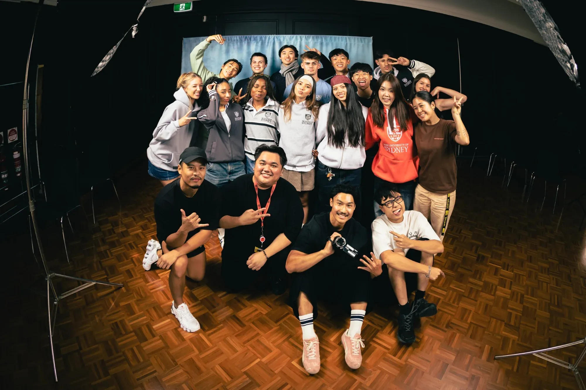 A large group in USU merchandise poses together on a wooden stage floor