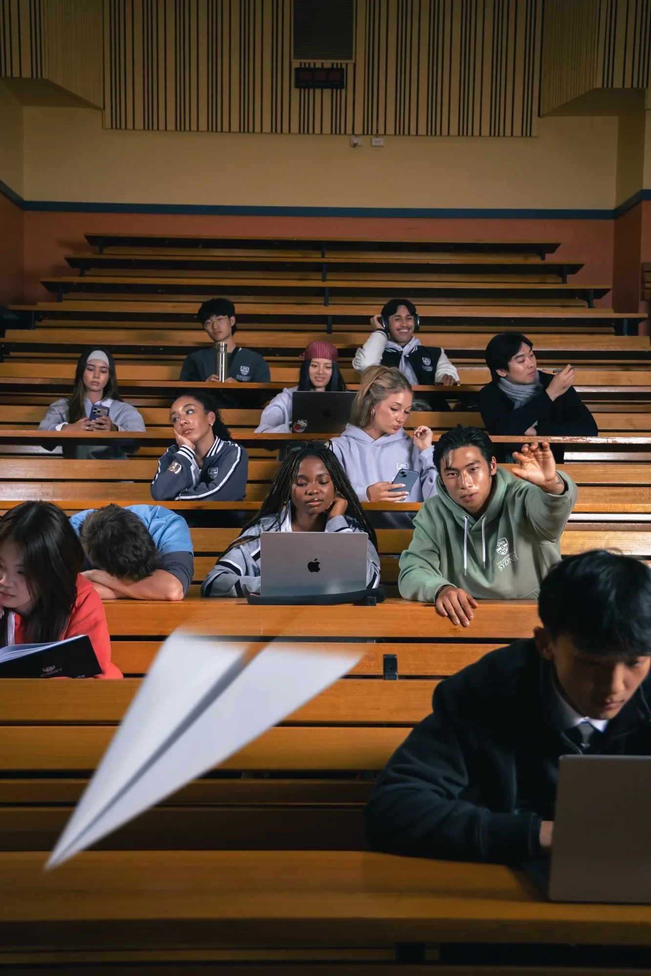 Students in a tiered lecture theatre, a paper plane flying past in the foreground