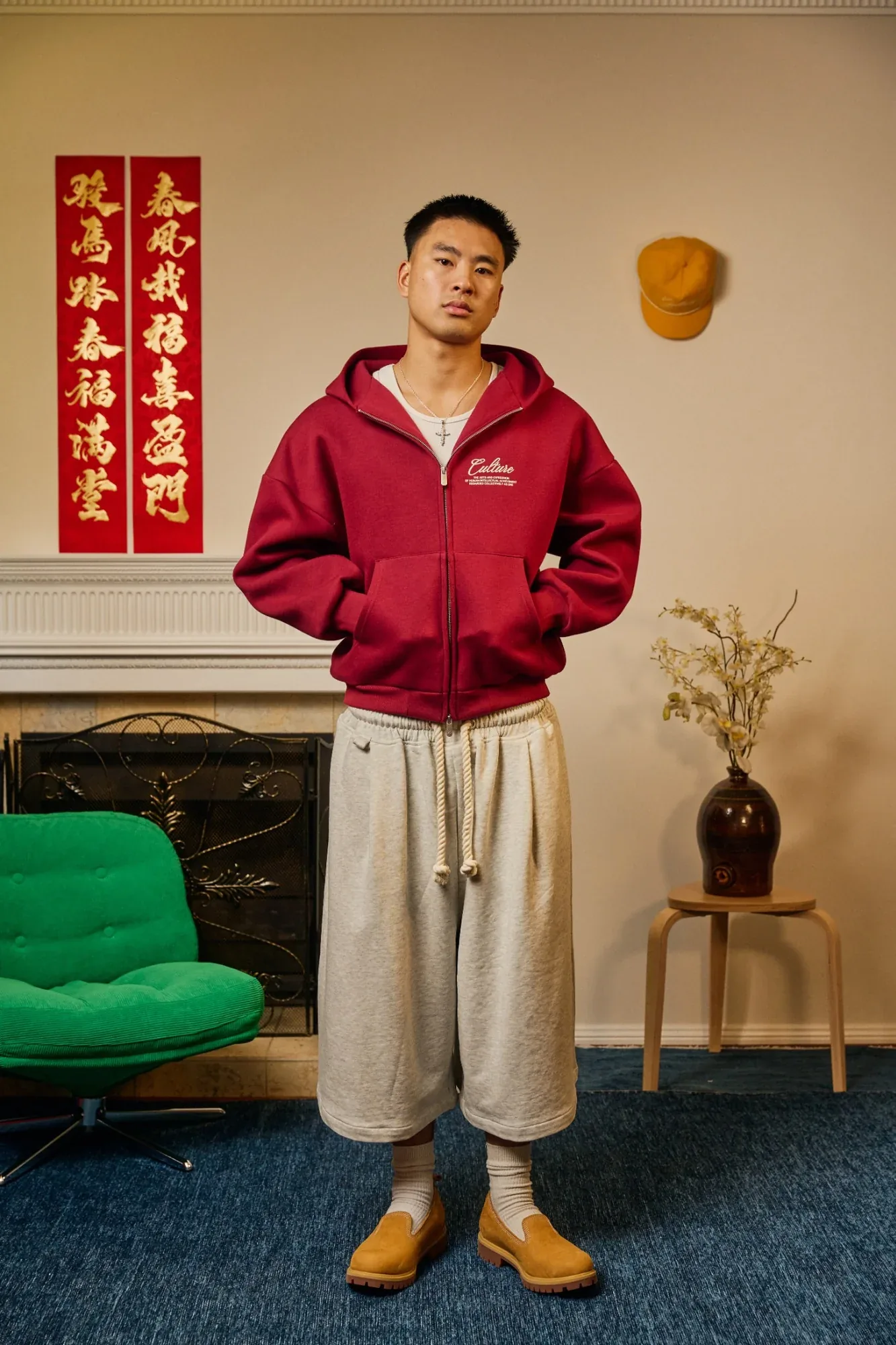 A model in a red Zone Four hoodie and wide cream trousers stands in a living room dressed for Chinese New Year