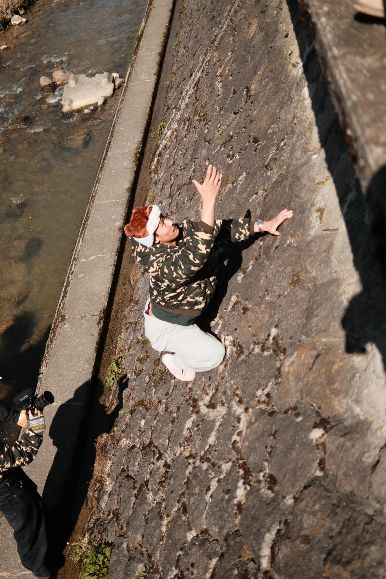 Shot from above, a model in a camo jacket leaps along the stone wall of a narrow channel